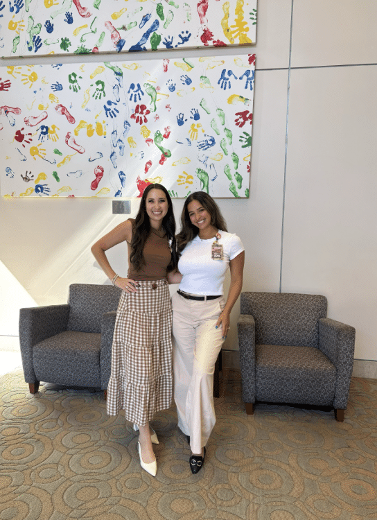 Briana Powell standing with another woman beneath colorful handprint artwork